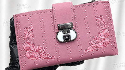 Pink wallet with floral embroidery held by a gloved hand against a white background