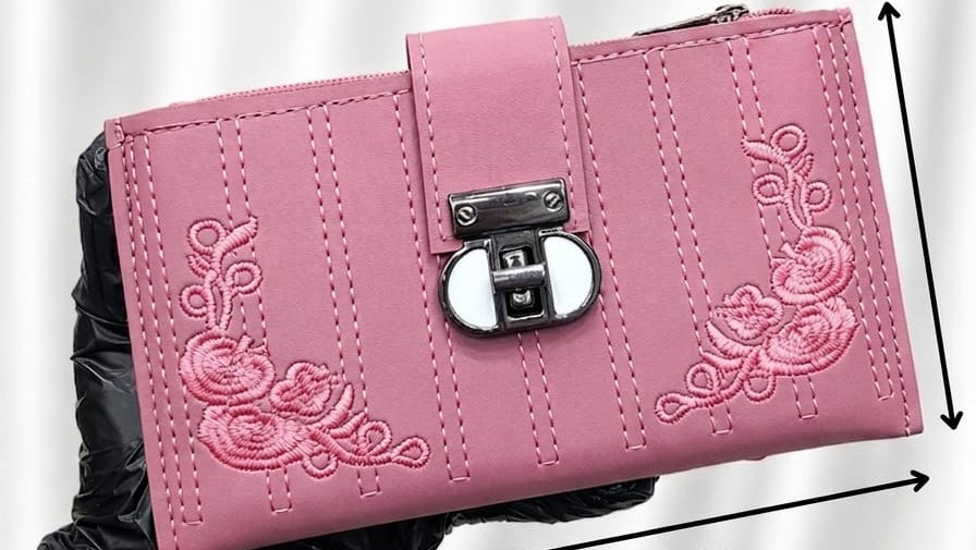 Pink wallet with floral designs held by a gloved hand, measurements indicated.