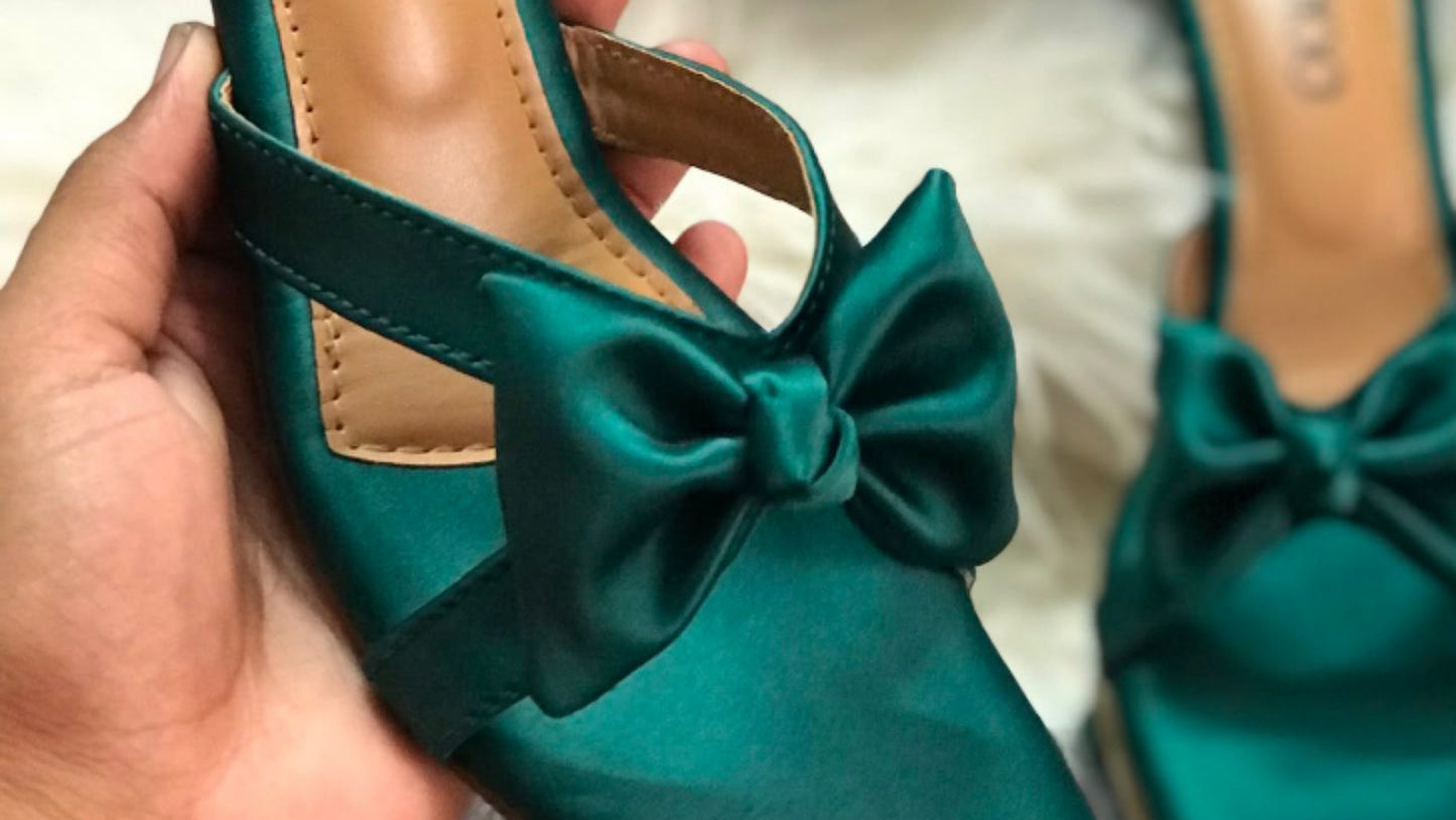 Teal high-heeled shoes with a bow held by a hand, brand name visible.
