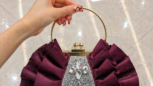 Purple handbag with decorative elements held by a hand against a reflective surface.