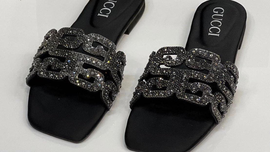 Black Gucci sandals with glittery design on a white surface with a Gucci box in the background.