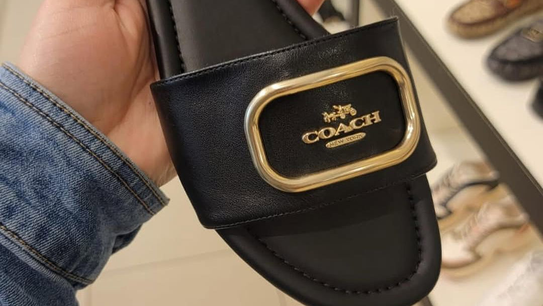 Black Coach sandal held in a hand with store interior in the background