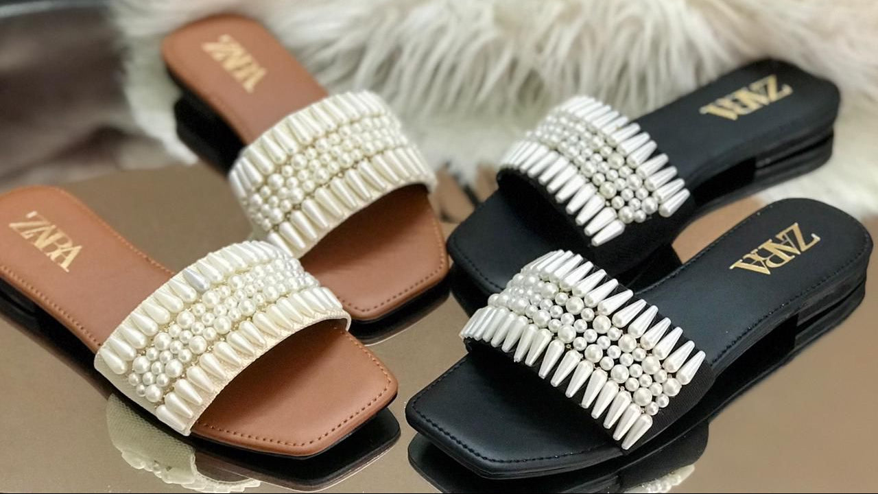 Pair of pearl-embellished slides with 'Zara' branding on a fluffy white surface.