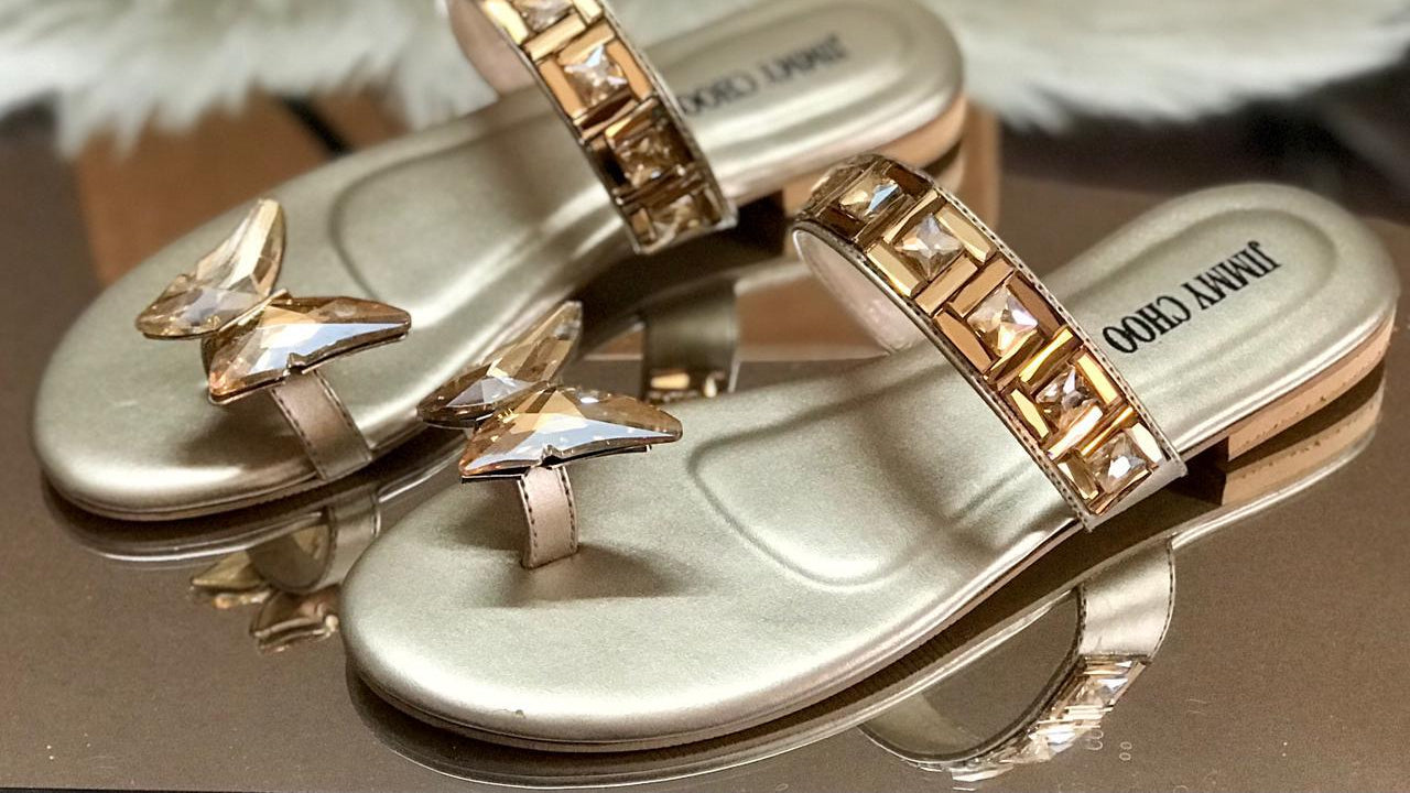 Gold sandals with butterfly designs on a reflective surface