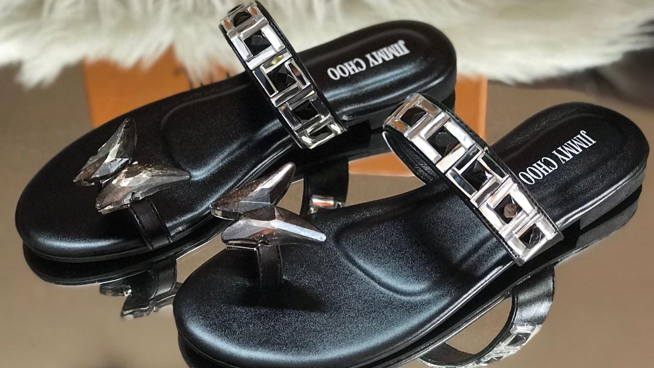 Black sandals with silver buckles on a reflective surface, with a blurred background.