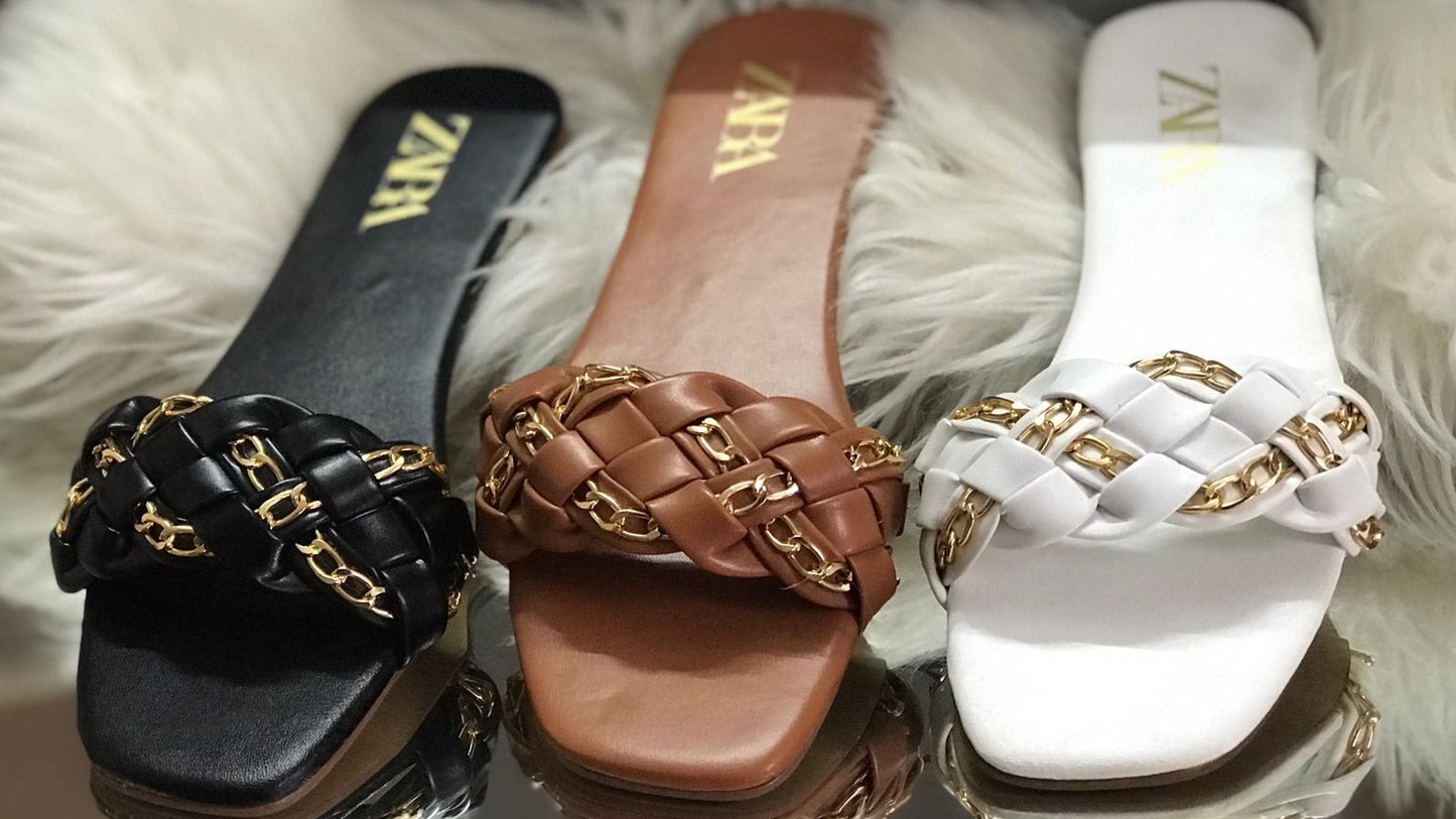 Three Zara sandals in black, brown, and white with gold chain details on a fluffy white surface.