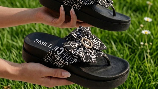 Black sandals with white patterns held by a person on grass