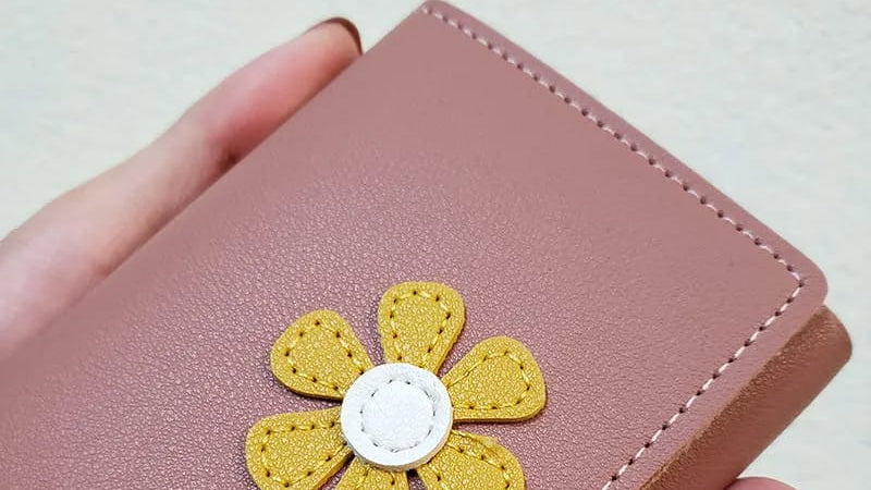 Pink wallet with a yellow flower design held by a hand on a light background