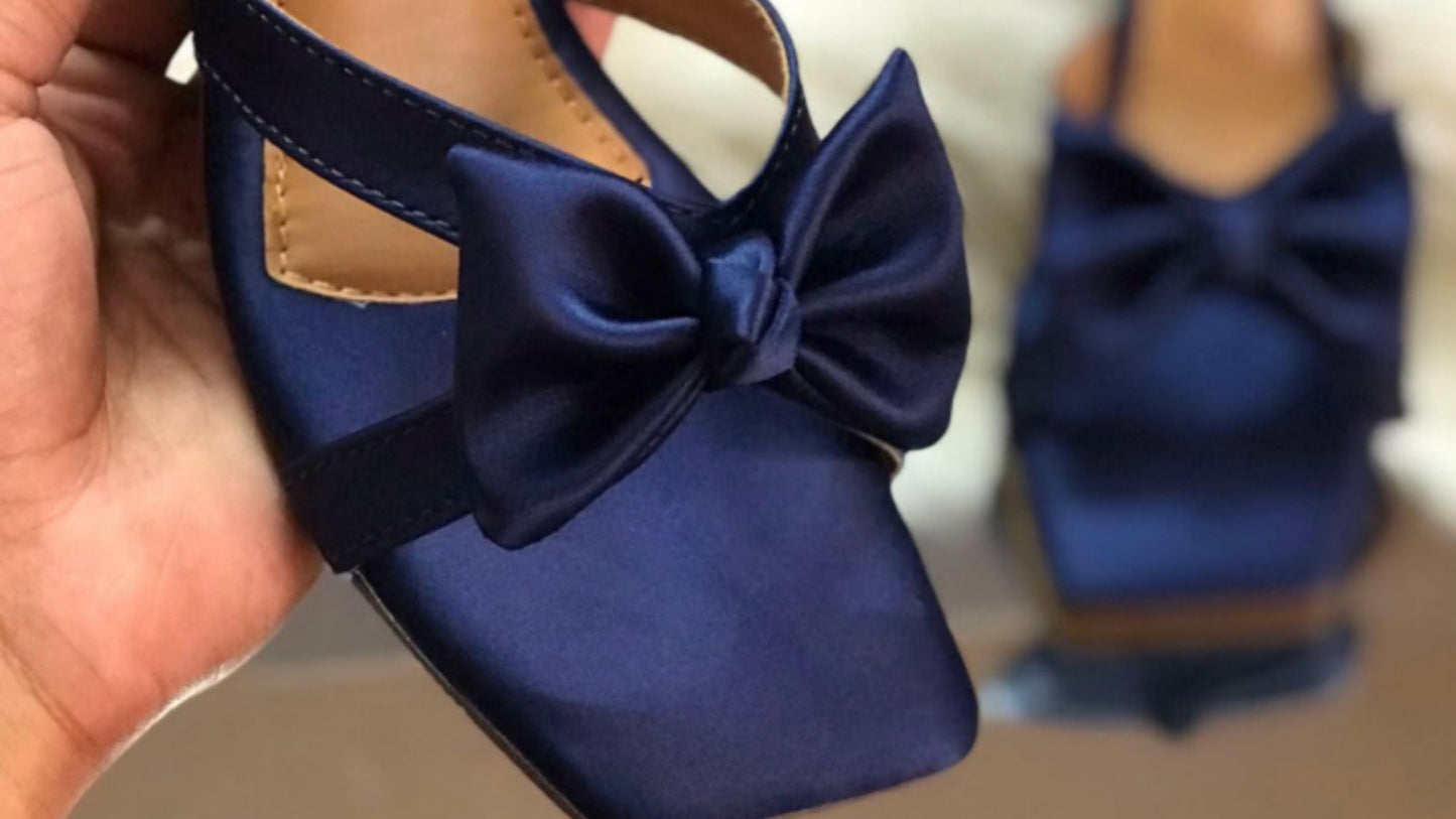 Blue sandal with bow held by a hand, brand 'Jimmy Choo' visible