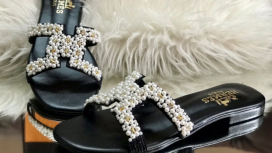 Black sandals with pearl embellishments on a fluffy white surface with an Hermès box in the background.