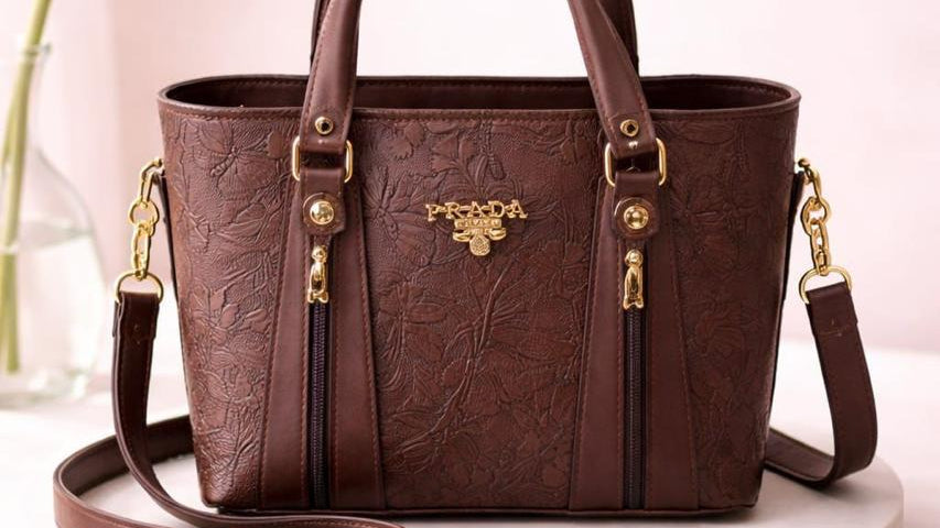 Brown leather handbag with gold accents on a white platform
