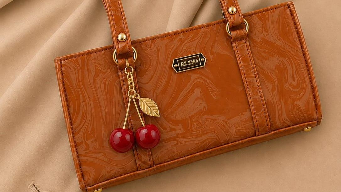 Brown handbag with cherry charm on a beige fabric background