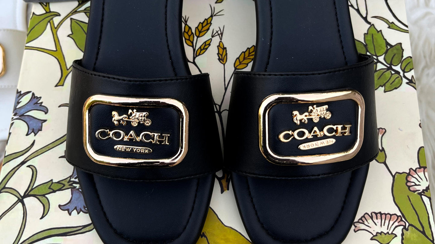 Black Coach sandals with gold logo on a patterned surface