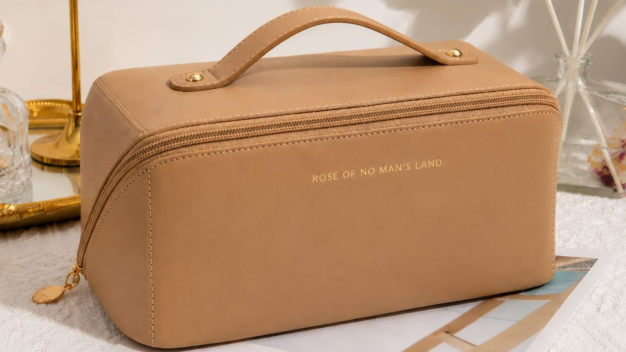 Brown cosmetic bag with 'Rose of No Man's Land' branding on a magazine with a plant and lamp in the background.