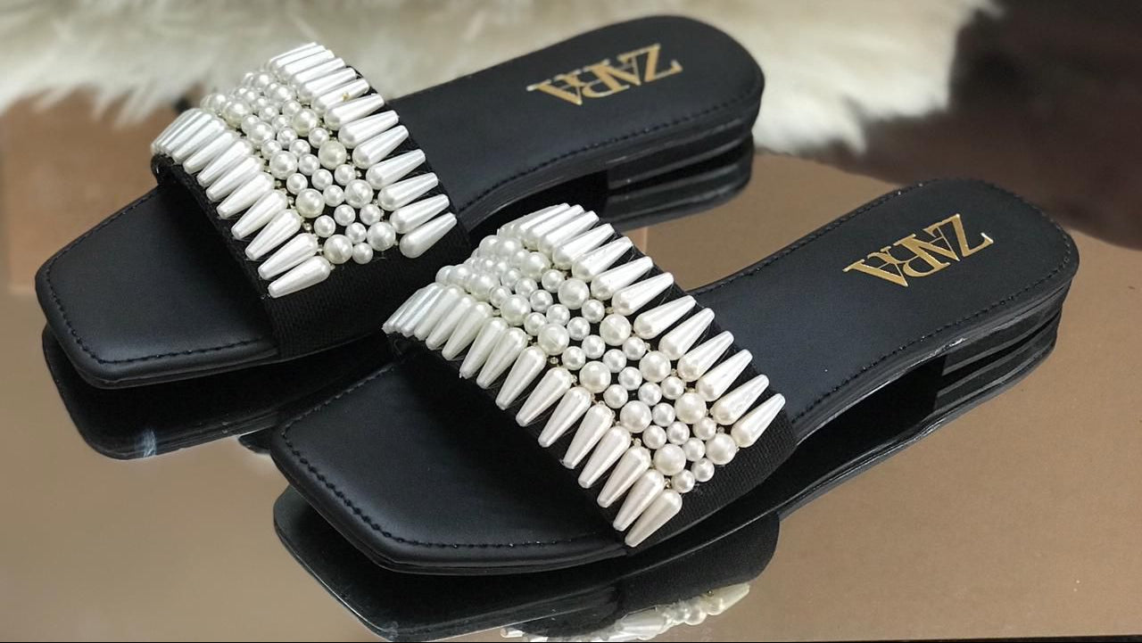 Black slides with white bead embellishments on a reflective surface.