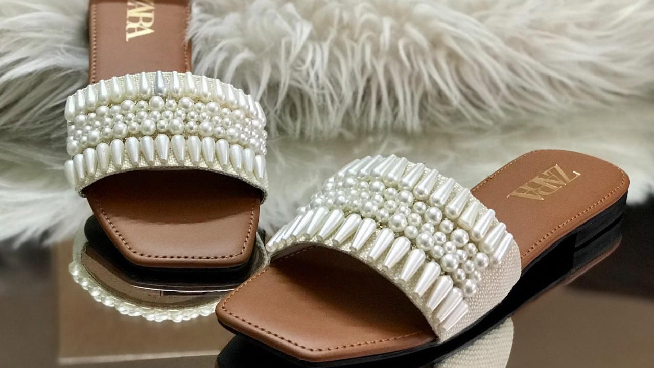 Pearl embellished slides with Zara branding on a fluffy white surface.