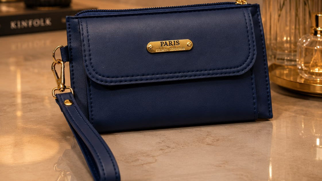 Blue clutch bag with 'PARIS' label on a reflective surface with decorative items in the background