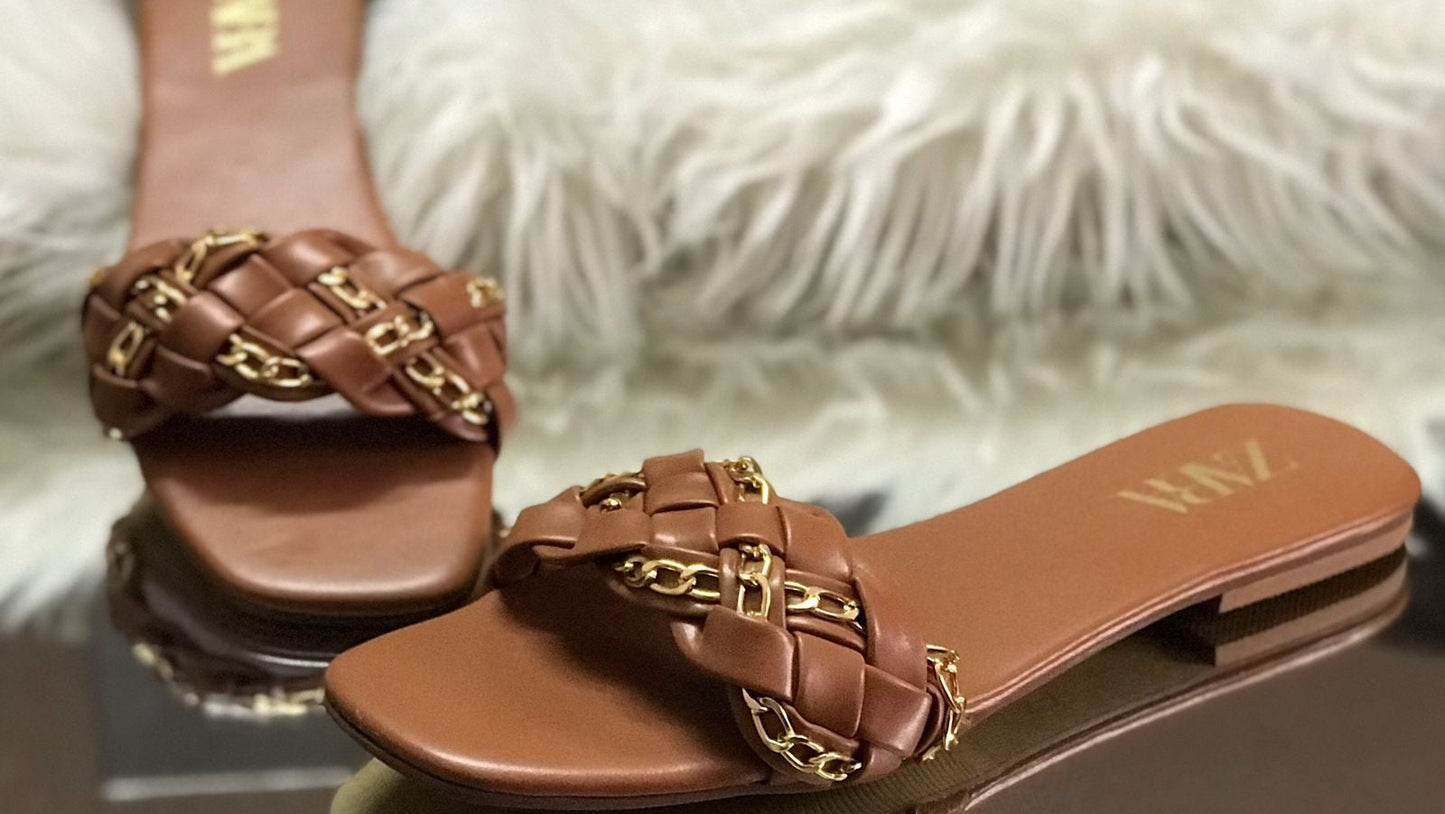 Brown sandals with gold chain detail on a fluffy white surface with Zara branding.
