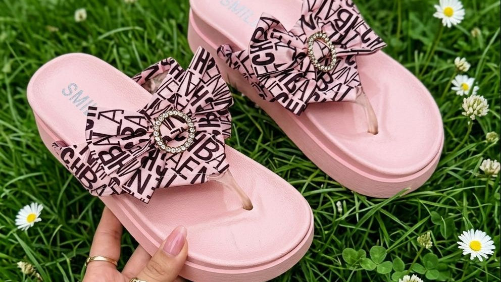 Pink sandals with decorative bows held on grass