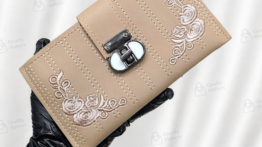 Beige wallet with floral embroidery held by a gloved hand against a white background