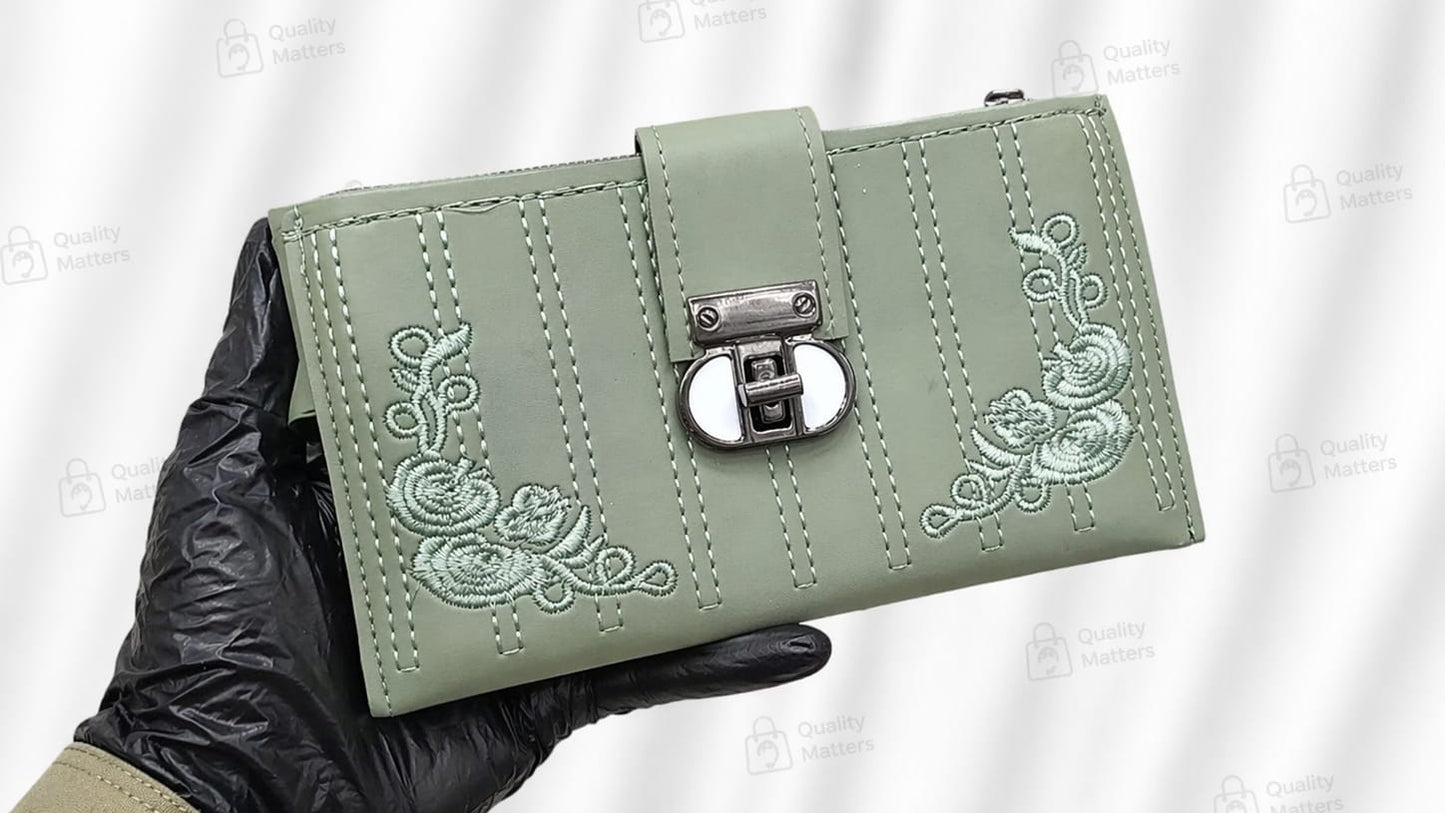 Green wallet with floral embroidery held by a gloved hand against a white background