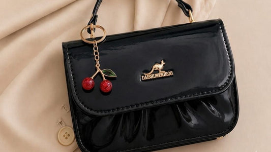 Black handbag with cherry charm on a beige fabric background