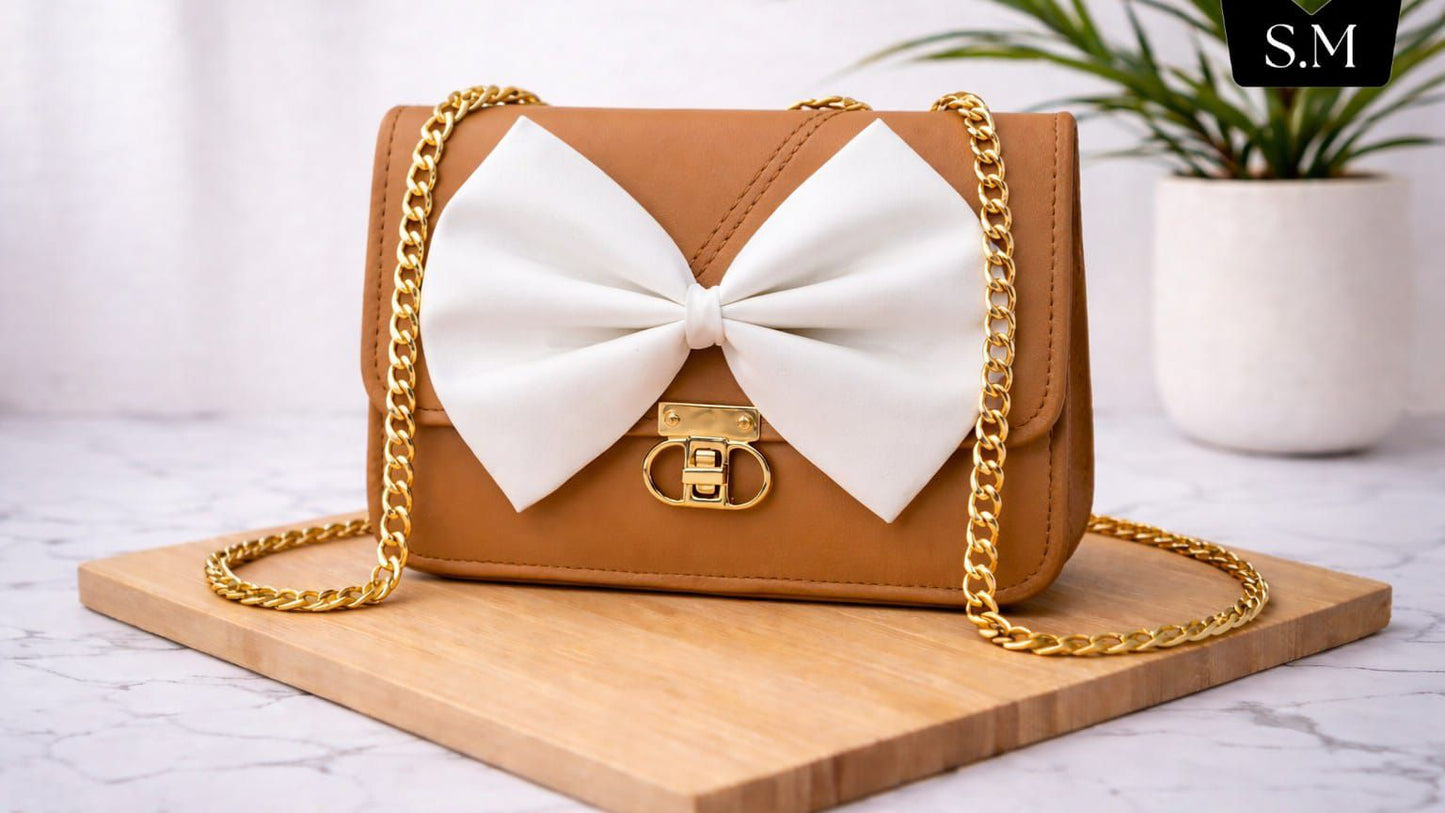 Brown handbag with a large white bow on a wooden board, plant in the background