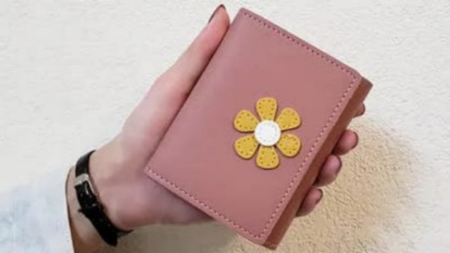 Pink wallet with a yellow flower design held by a hand on a light background