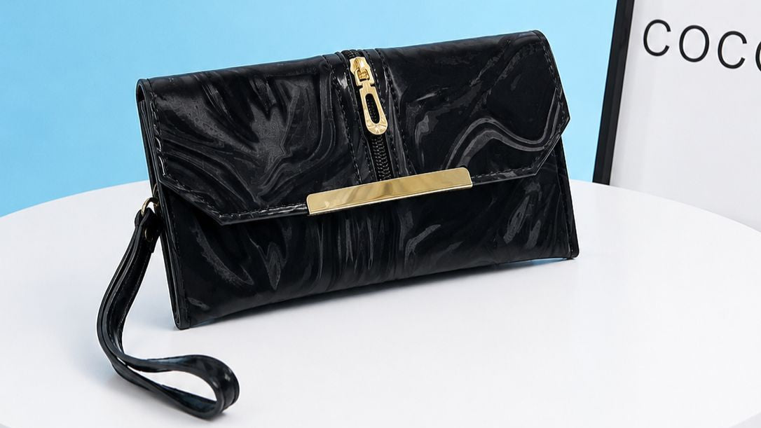 Black clutch bag with gold accents on a white surface with a light blue background