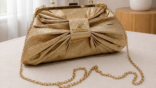 Gold clutch bag with a bow design on a light surface with a neutral background