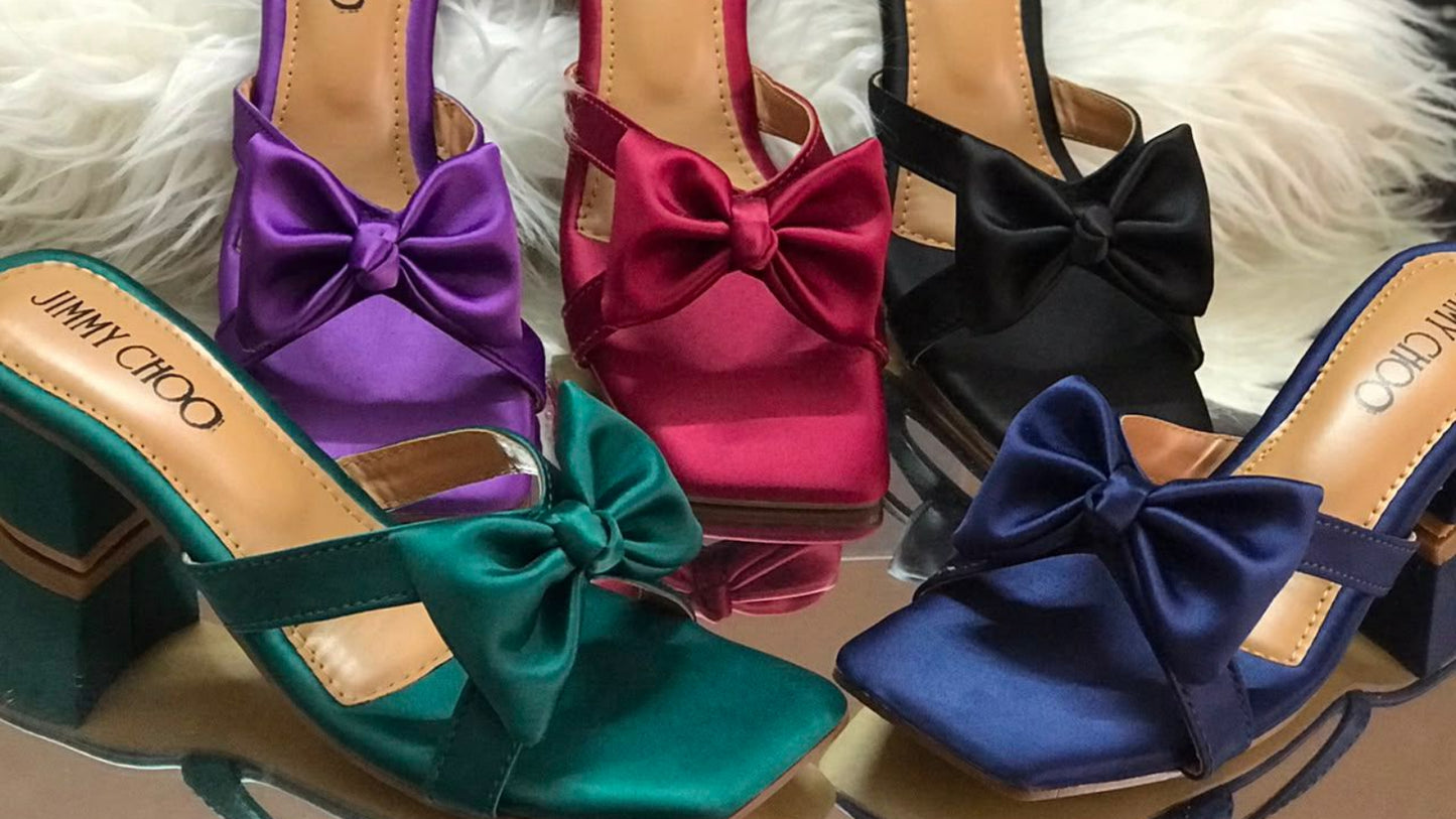 Colorful Jimmy Choo sandals with bows on a fluffy white surface