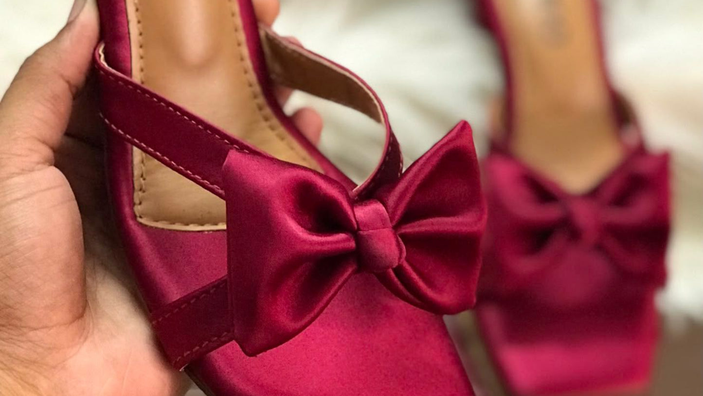 Red high-heeled shoes with a bow held by a hand, brand 'Jimmy Choo' visible.