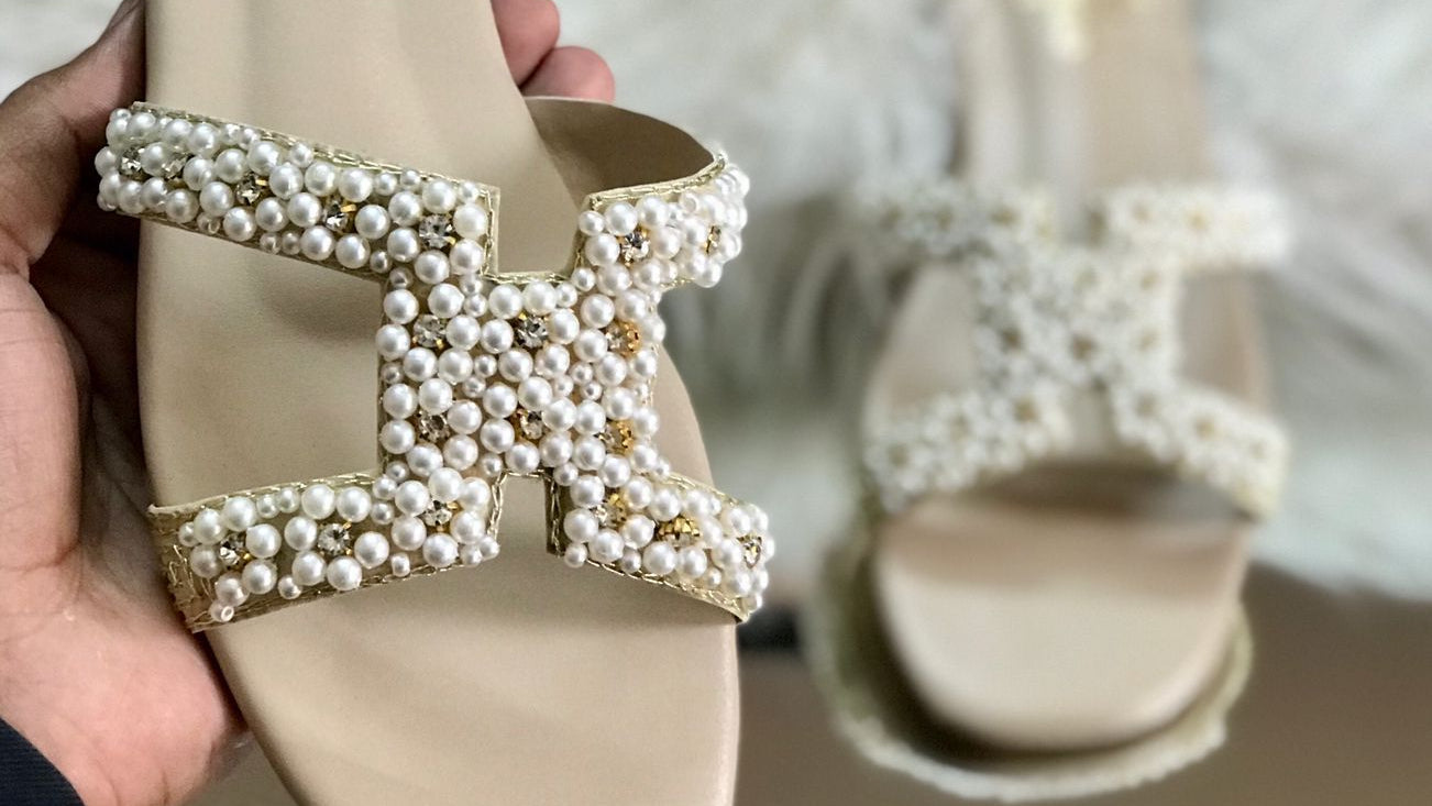 Beige sandal with pearl embellishments held by a hand, Hermes box in the background