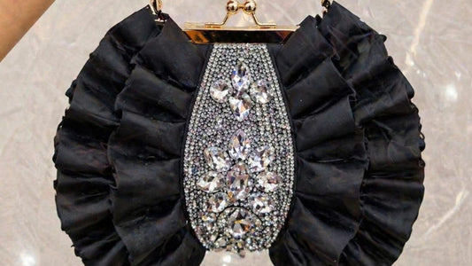 Black ruffled handbag with a decorative clasp held by a hand against a sparkling background.