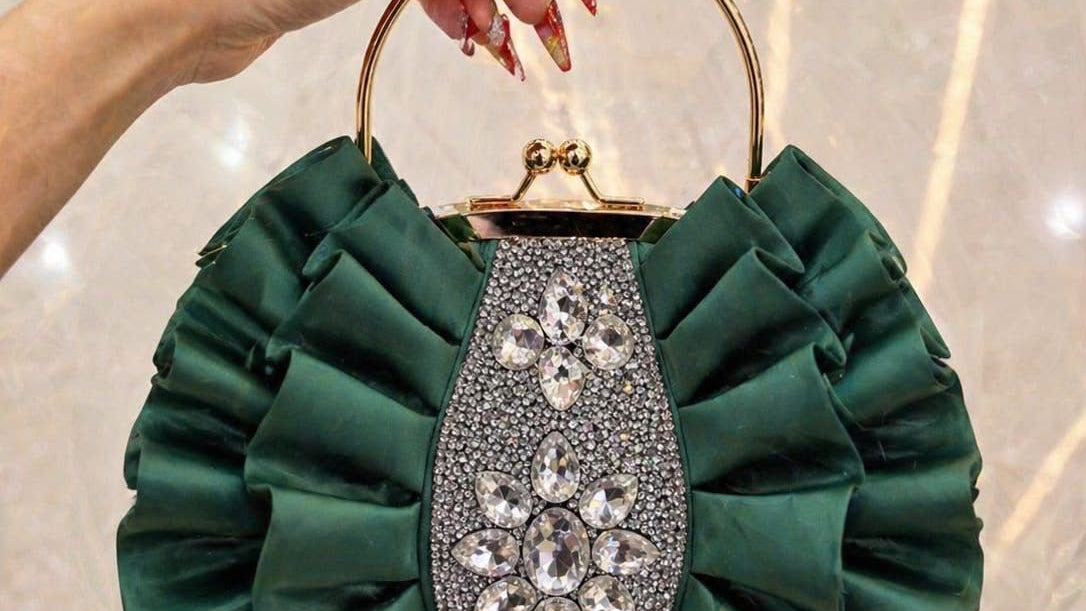 Green handbag with decorative handle held by a hand against a neutral background