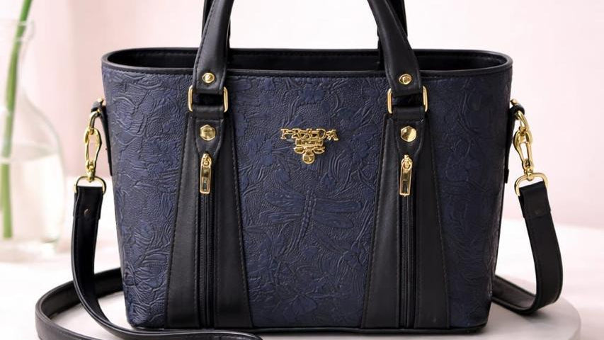 Blue handbag with gold accents on a white platform
