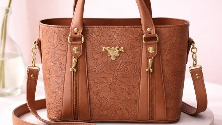 Brown leather handbag with gold accents on a white platform