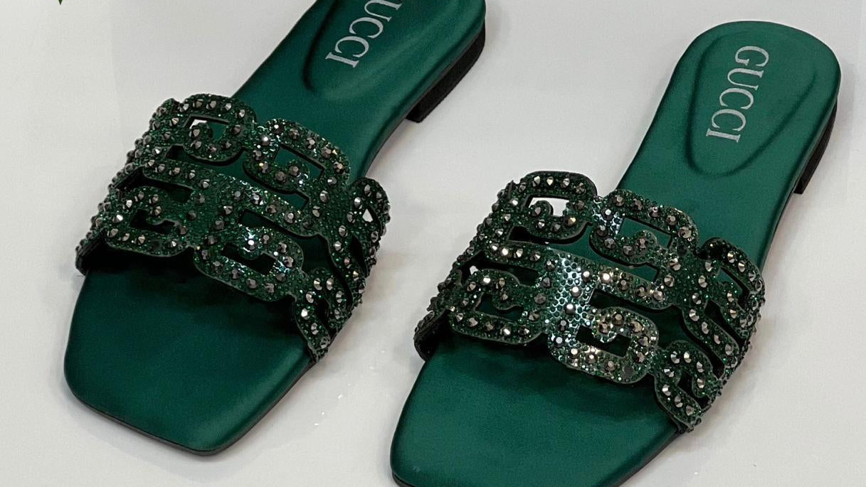 Green Gucci sandals with embellishments on a white background with a Gucci box and red rose.