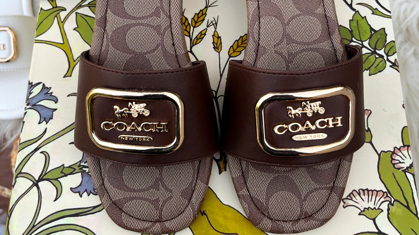 Pair of Coach sandals with logo on a floral-patterned surface