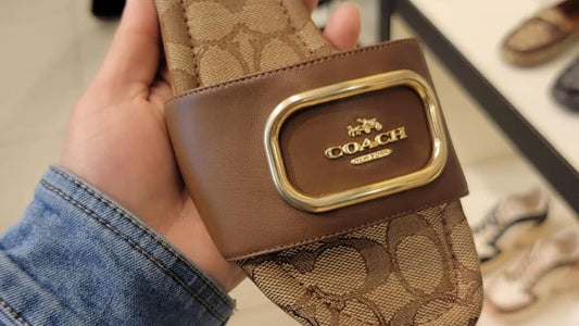 Coach sandal held by a hand with store shelves in the background