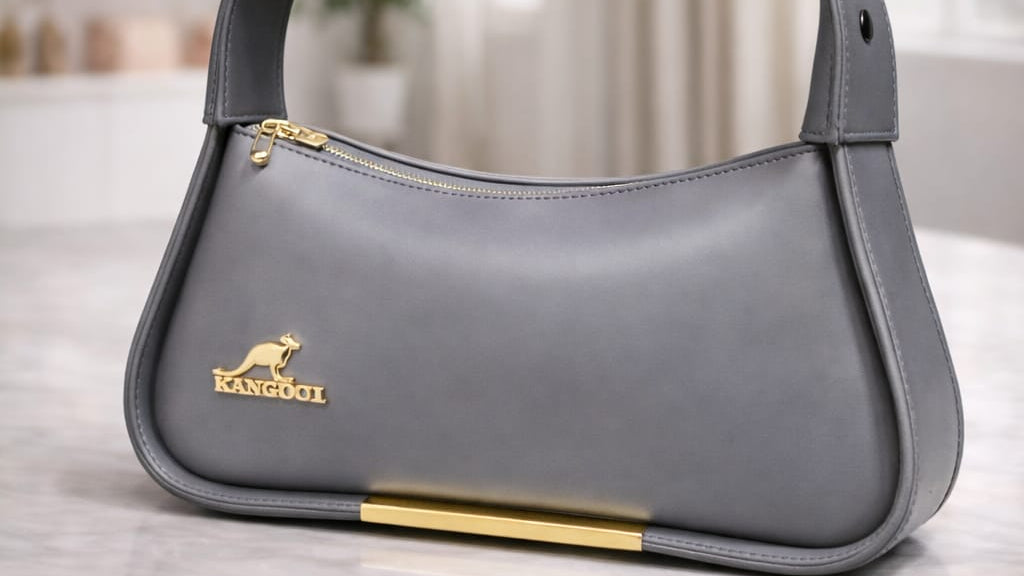 Gray handbag with a gold zipper on a marble surface, with a blurred background of shelves and decor.