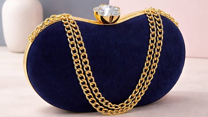 Navy blue clutch bag with gold chain and decorative clasp on a light pink surface, with 'JUST For YOU' branding.