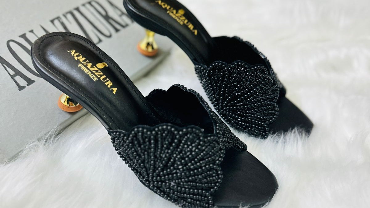 Black beaded sandals on a white fur surface with a magazine underneath.