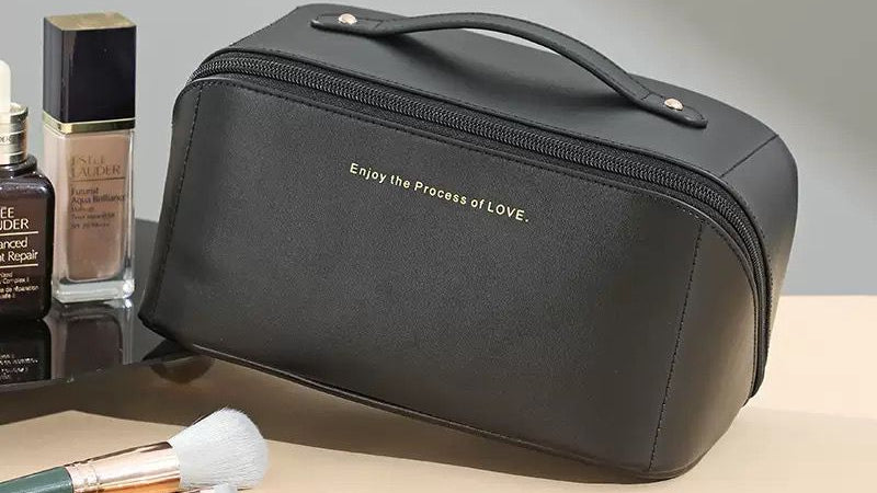 Black cosmetic bag with makeup brushes and products on a neutral background