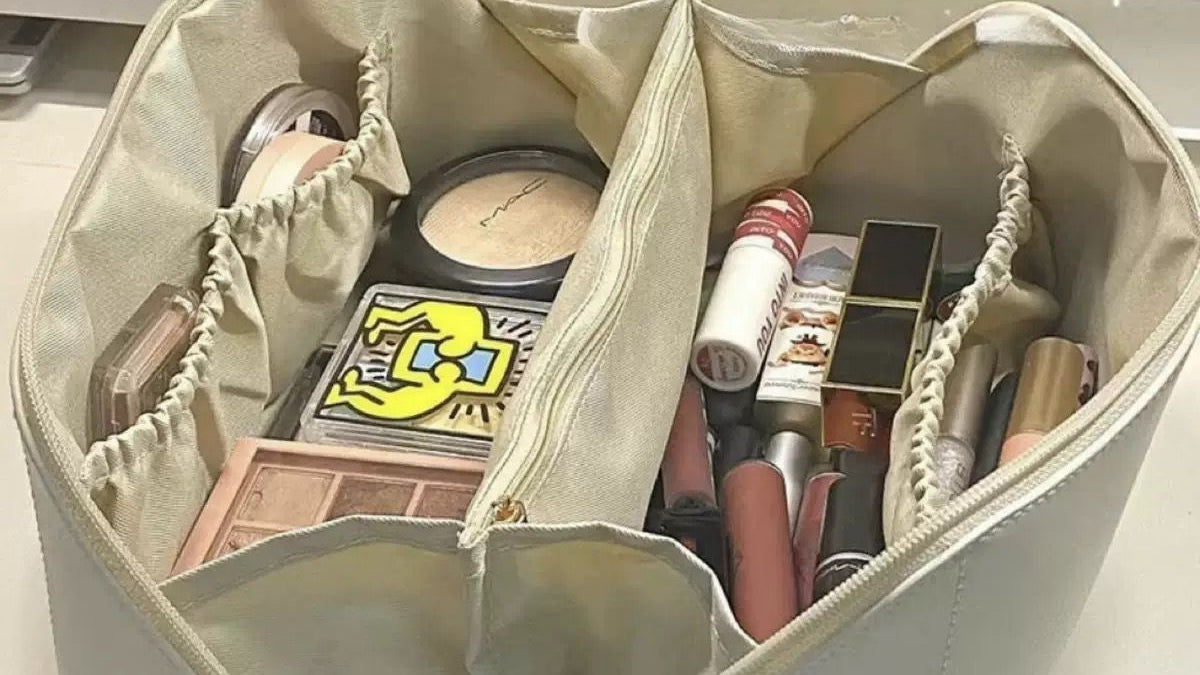 Beige cosmetic bag with various makeup items on a light gray surface
