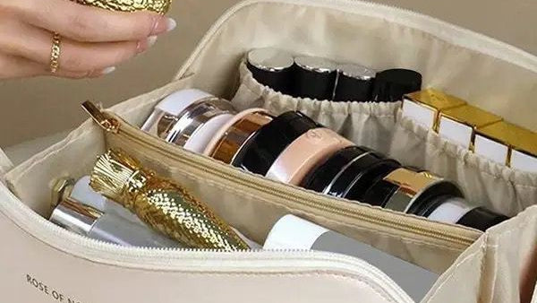 Beige makeup bag with cosmetic items and a hand holding a gold container.