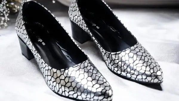Pair of silver and black patterned shoes on a white surface with decorative elements.